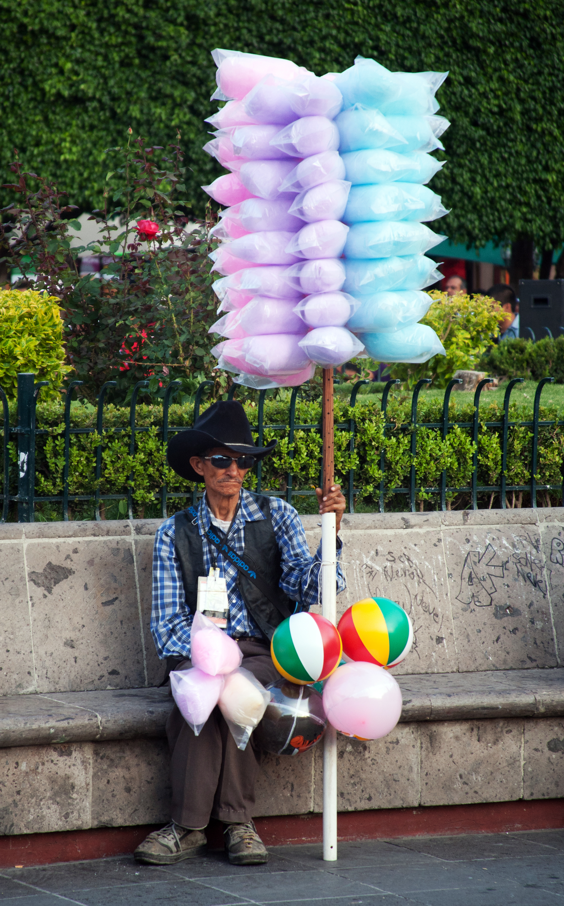 Mexican cotton candy ball on a stick being held in a plaza