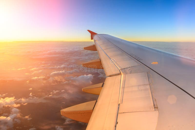 View of airplane wing from window seat above clouds, sunrise, aesthetic travel photography