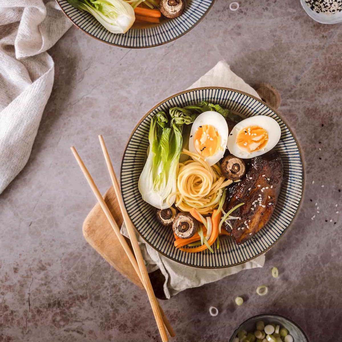 Steaming bowl of intricate ramen noodles with pork belly and egg, top down view, professional food photography