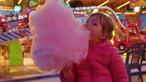 Happy american child eating giant blue cotton candy at a carnival, bright lights in background