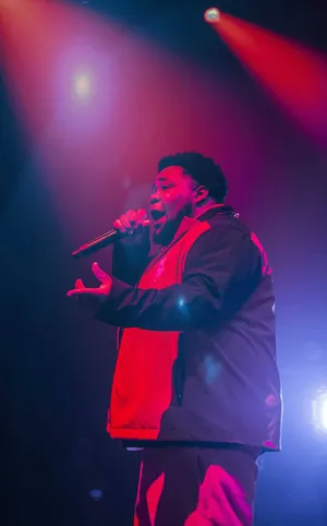 Rod Wave singing passionately into a microphone close up, sweat, emotion, dark moody background